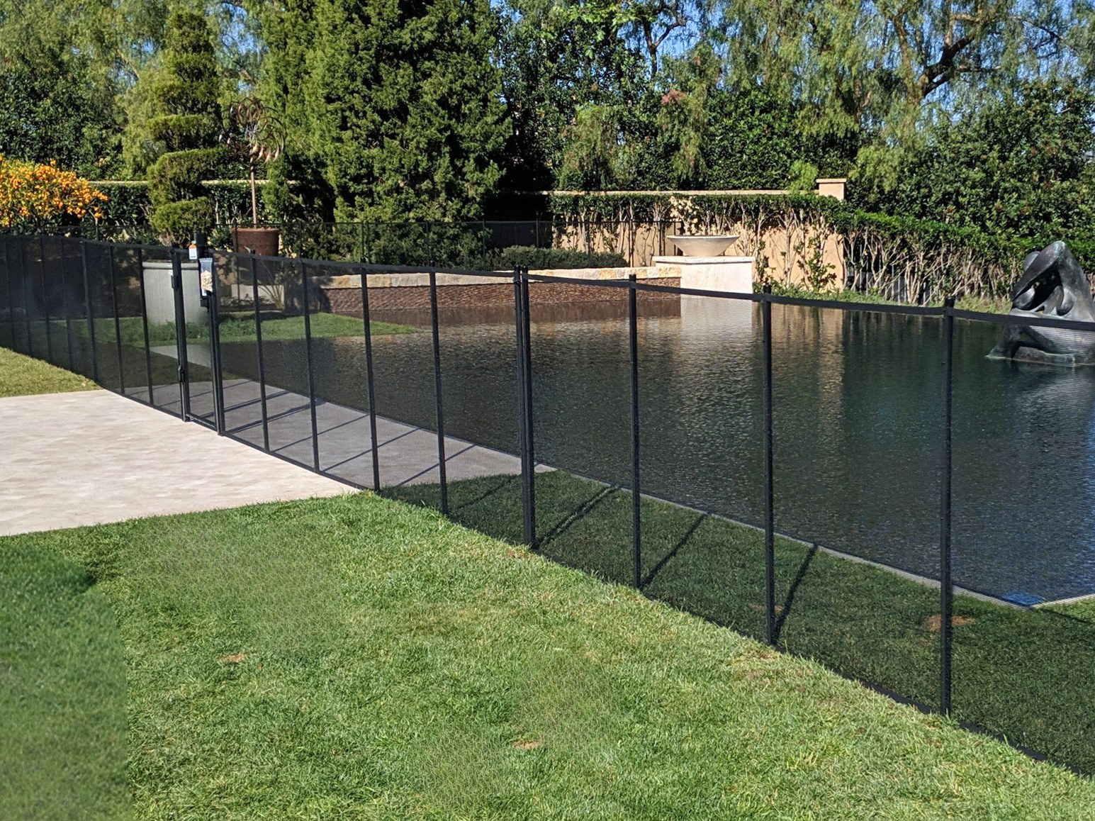 Removable mesh pool safety fence set into a lawn beside an infinity-edge pool in the greater Austin area, All-Safe certified
