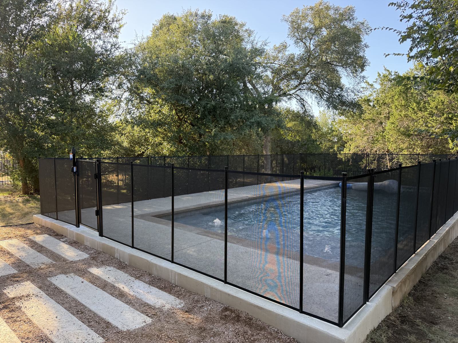 Removable mesh pool fence with a self-closing safety gate around a rectangular lap pool on a wooded acreage lot in Buda TX, All-Safe certified